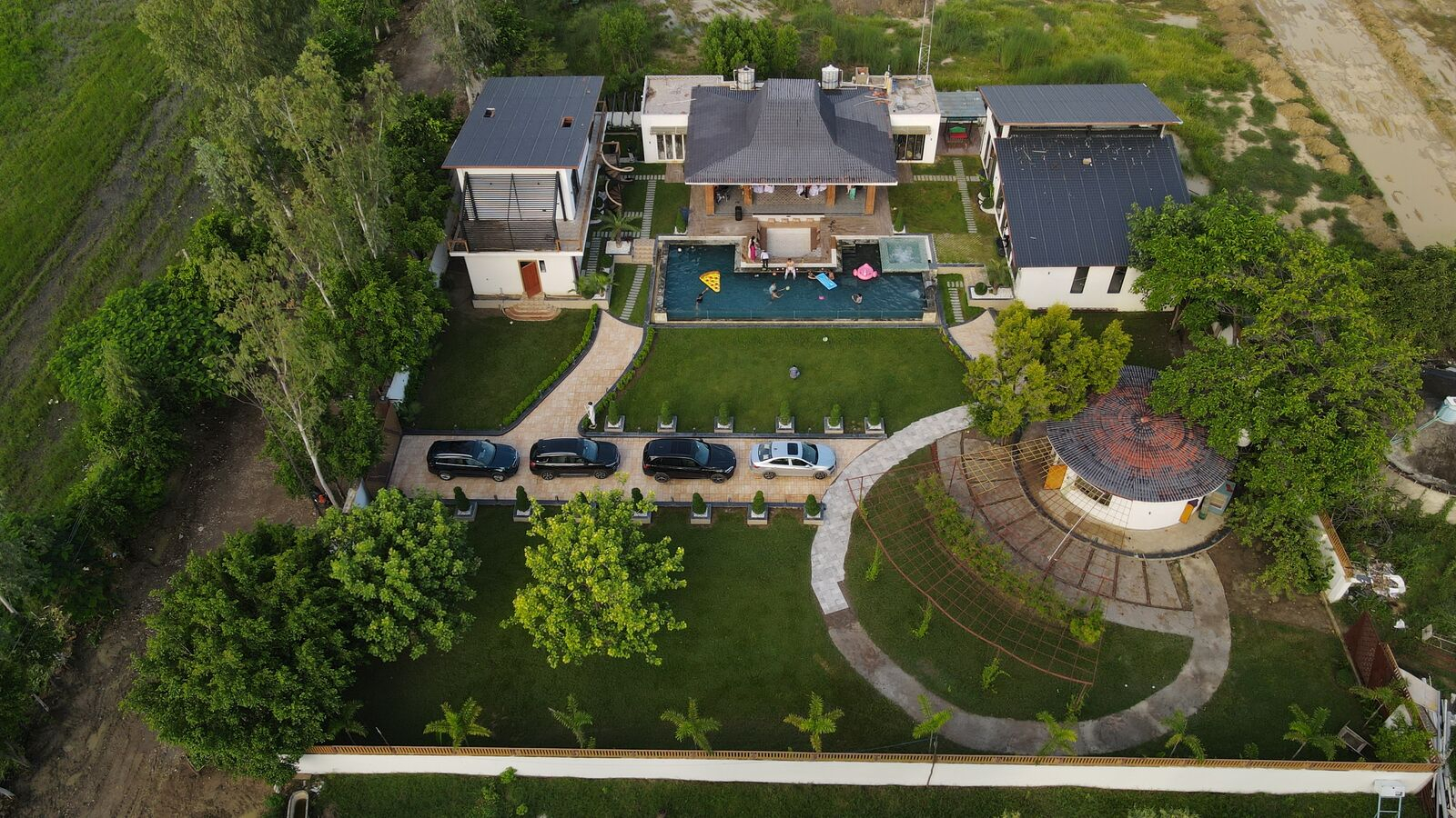 Aerial view of the 27,500 sqft Urban Euphoria private farmhouse estate — villa, pool, lawns and round Bali hut